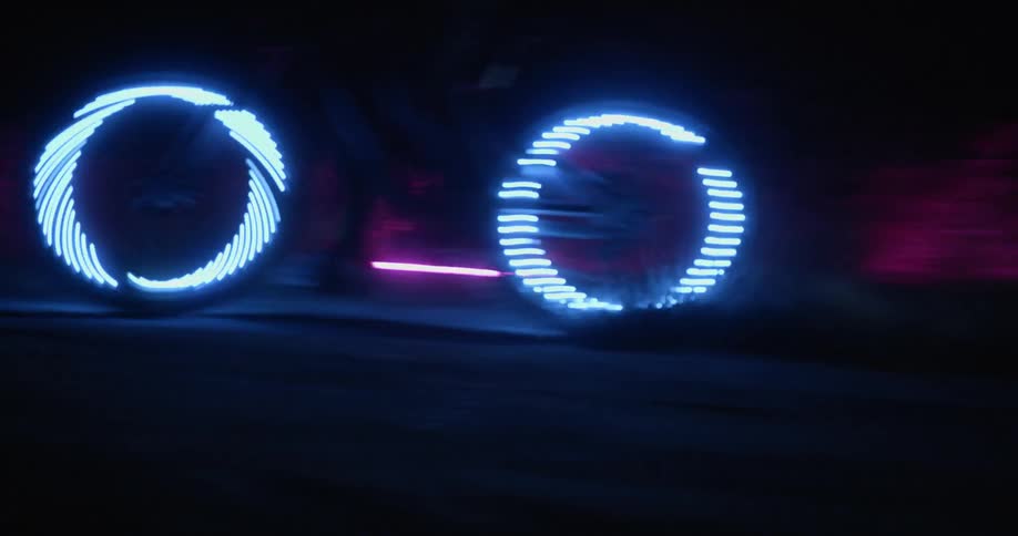 A person rides a bicycle equipped with blur lights on its wheels along a path in the darkness of night