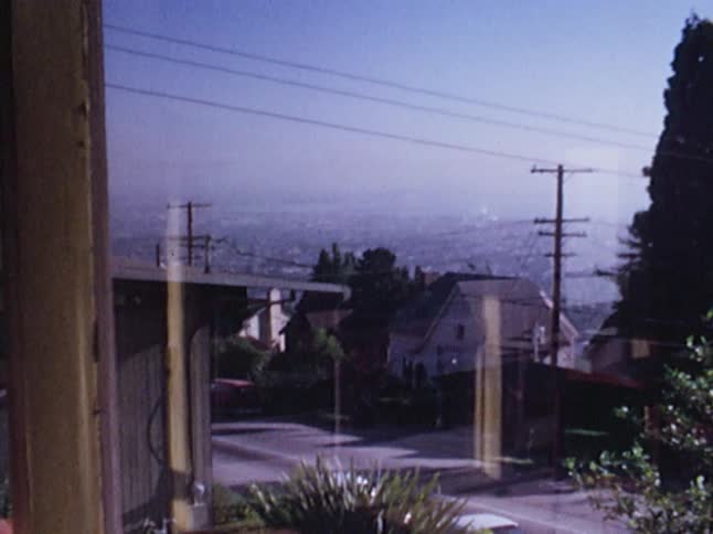 Old film footage of a dining area, balcony and view looking down over a city covered in haze