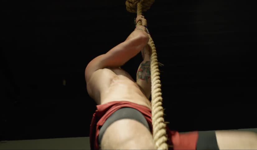 Shirtless man on gym climbs rope