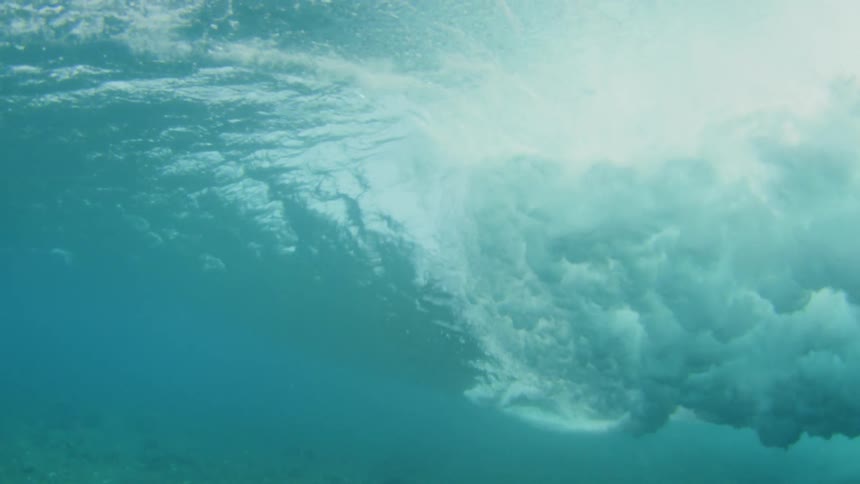 From beneath the surface of the ocean waves can be seen rolling overhead and crashing downward to cause churning and bubbling water
