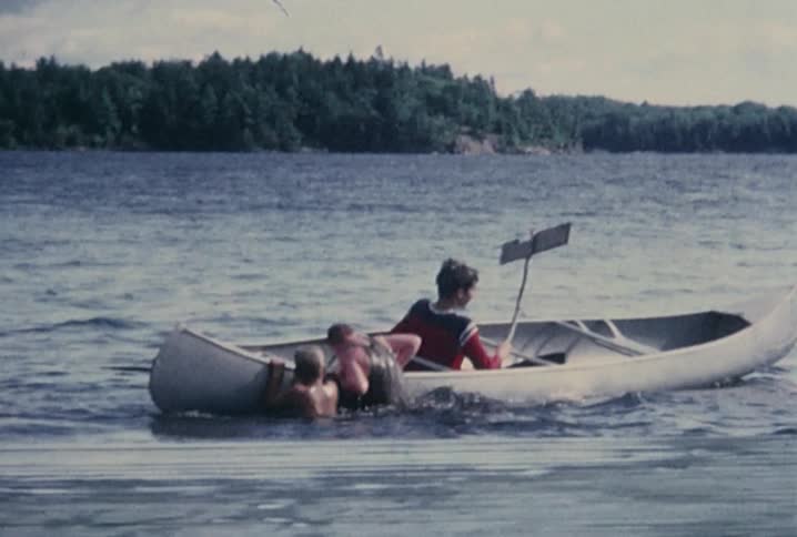 Boys reach out of the water and tip over a canoe