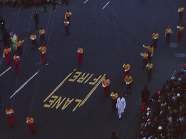 Old footage of a large popeye balloon being held by several people as they walk down the street during a parade in a city