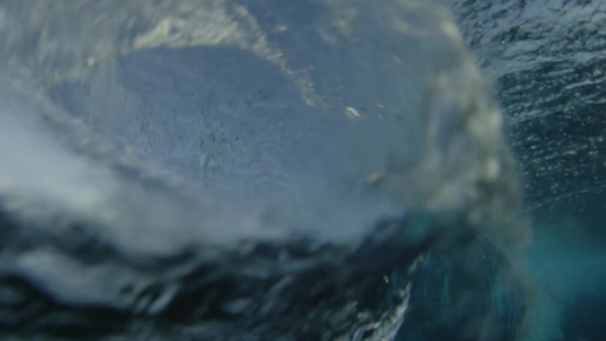 A large wave rushes forwards and curls over on itself under a beautiful blue sky
