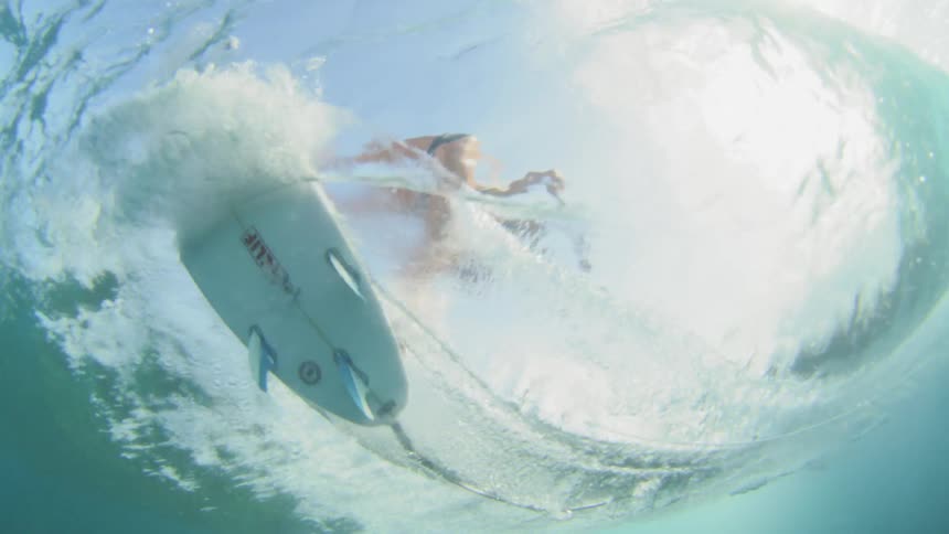 From beneath the ocean surface a female surfer can be seen swiftly surfing on a wave