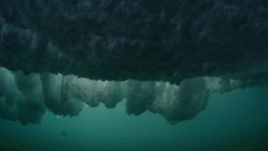 Wave crashes on surface under sunny sky and churns underwater