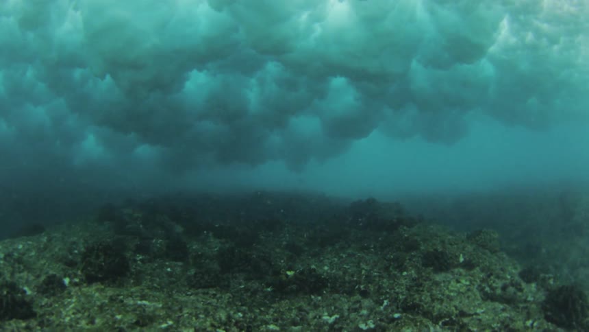 From underneath the surface of the ocean bubble can be seen where a wave is crashing down above the ocean floor