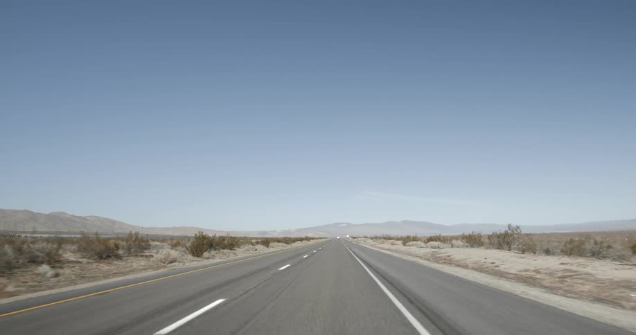 A paved two lane road extends through a dry and uninhabited desert landscape