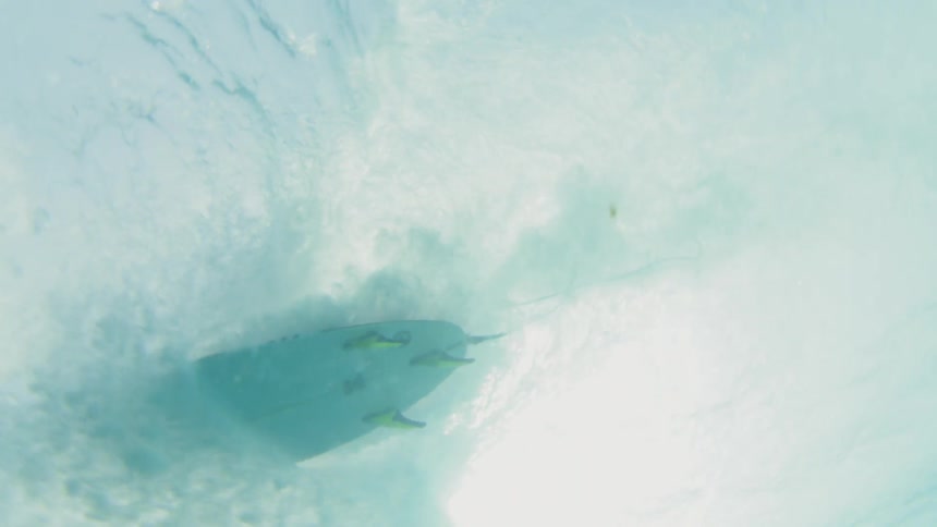 A surfboard traveling through the ocean is seen from below