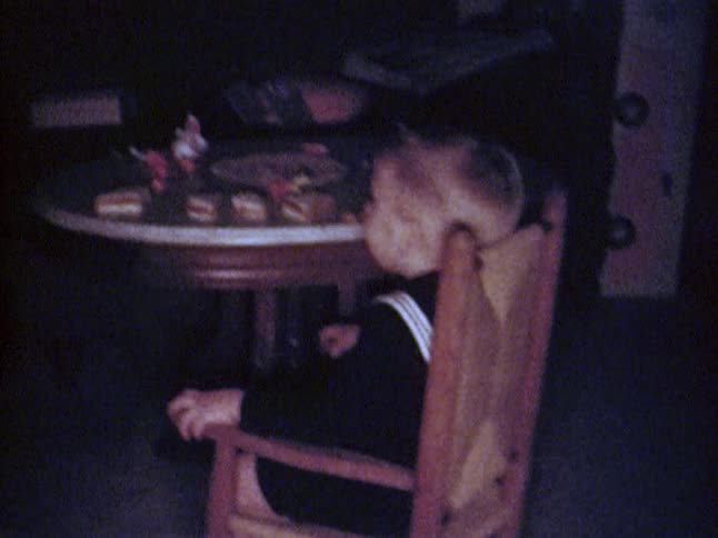 A boy picks up and carries his chair to a table and sits down