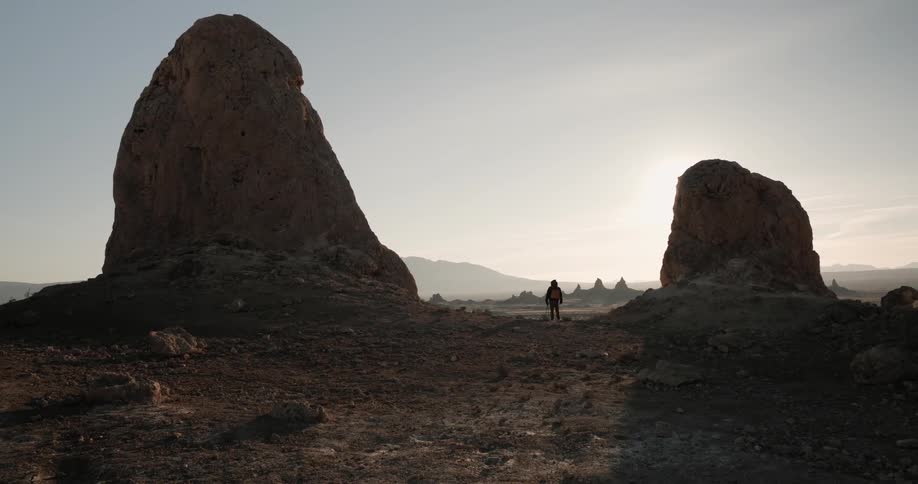 Man standing between two massive rocks on a desert at sunrise