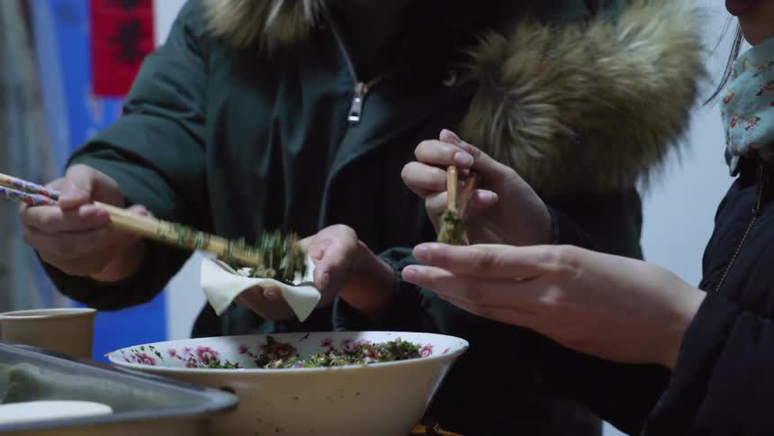 Two people holding chopsticks are scooping ingredients and placing them into small wraps
