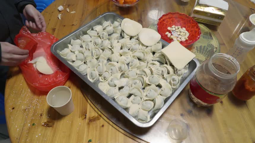 A man is preparing homemade dumplings on a metal tray over a table