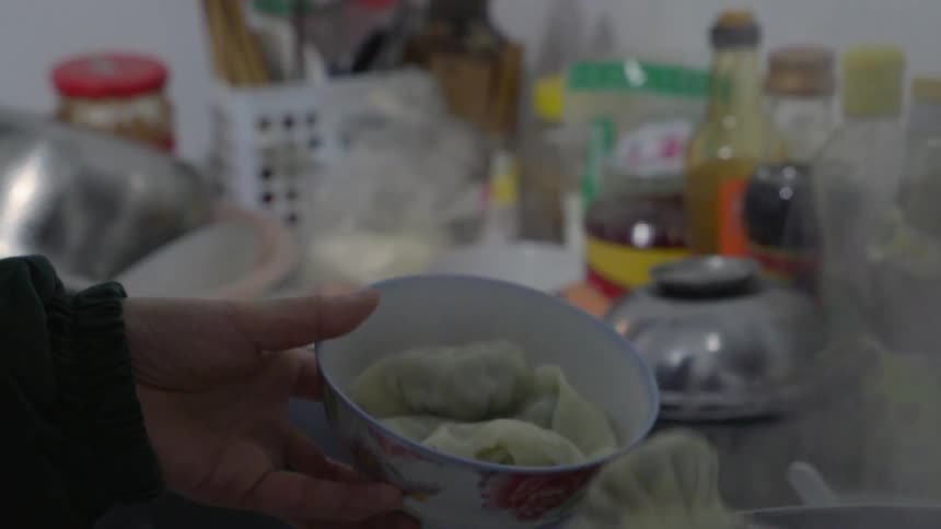 Person serving steaming dumplings from a pot to a bowl on a kitchen