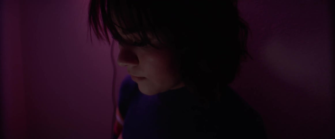 A young female sits in darkened room while looking down at an illuminated screen
