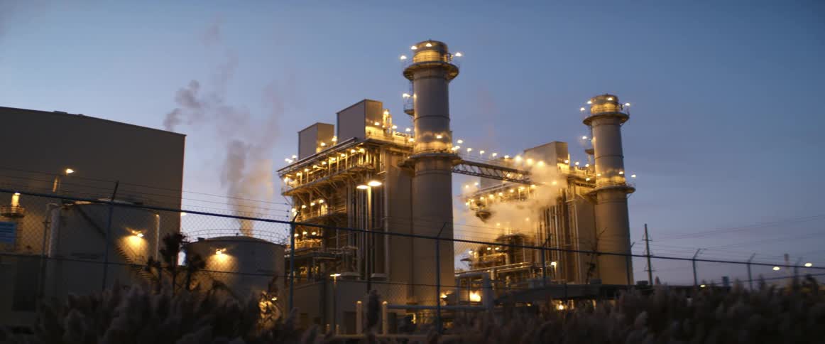 A large industrial facility is brightly illuminated against the evening sky