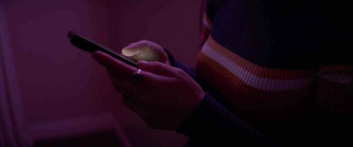 A woman in a sweater swipes the screen of her smart phone with her thumb in a darkened room