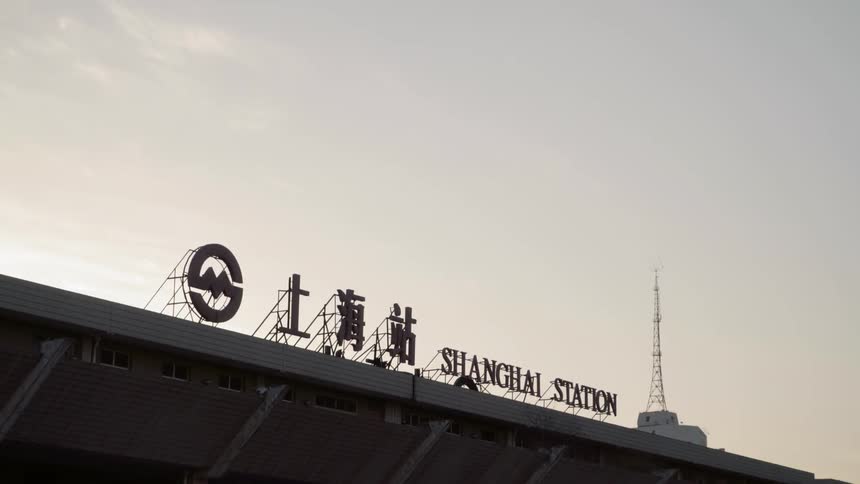 A sign on the top of a station with a large tower in the background
