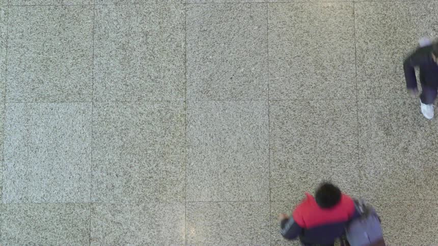 A person with a suitcase running on tiles while passing another person