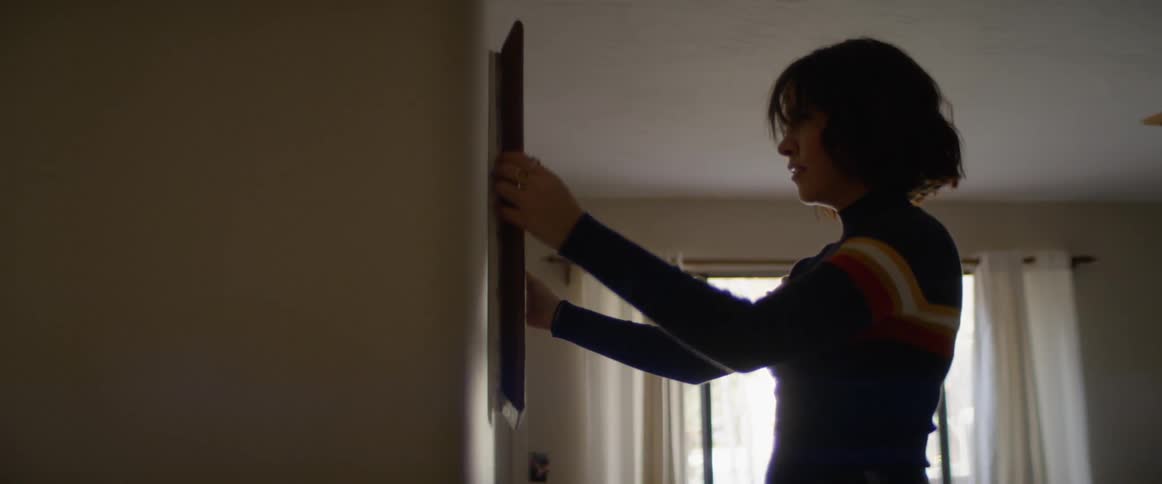 A woman adjusting a picture frame on a wall
