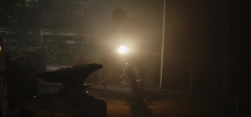 A man walks his motorcycle in to a garage and then sits on it