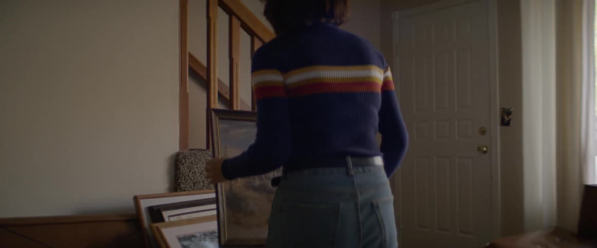 A woman picks a picture up off a table and goes to hang it on the wall