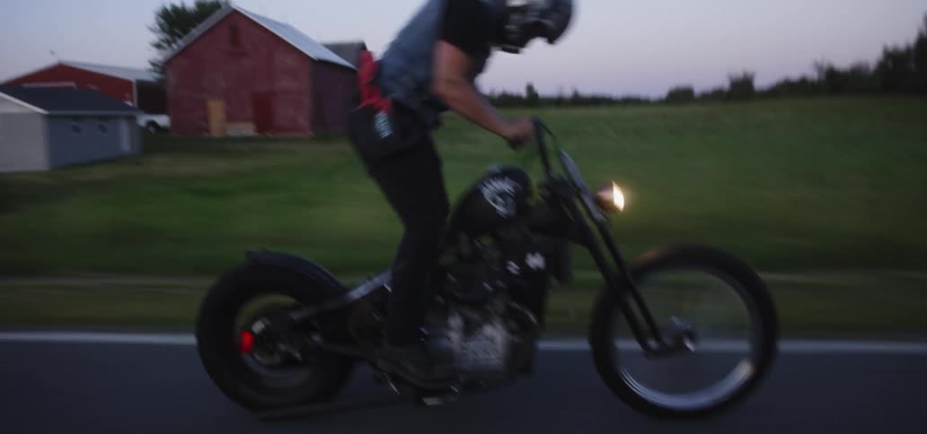 Man stands up while riding a motorcycle down a country road