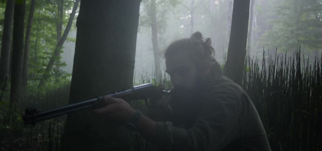 A man creeps through the woods and aims his gun