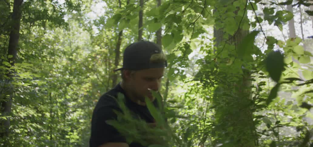Man angrily cuts bushes and plants with short machete in forest