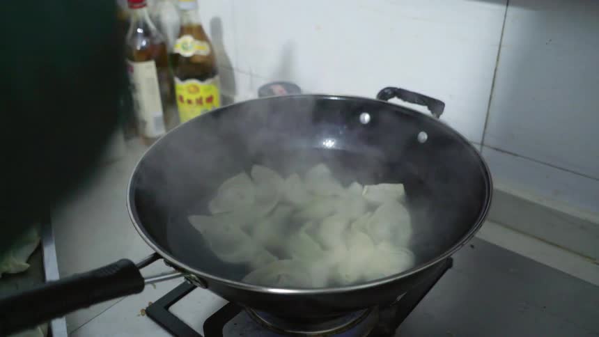 A cook is taking uncooked wontons from a baking sheet and placing them in a steaming hot wok to cook