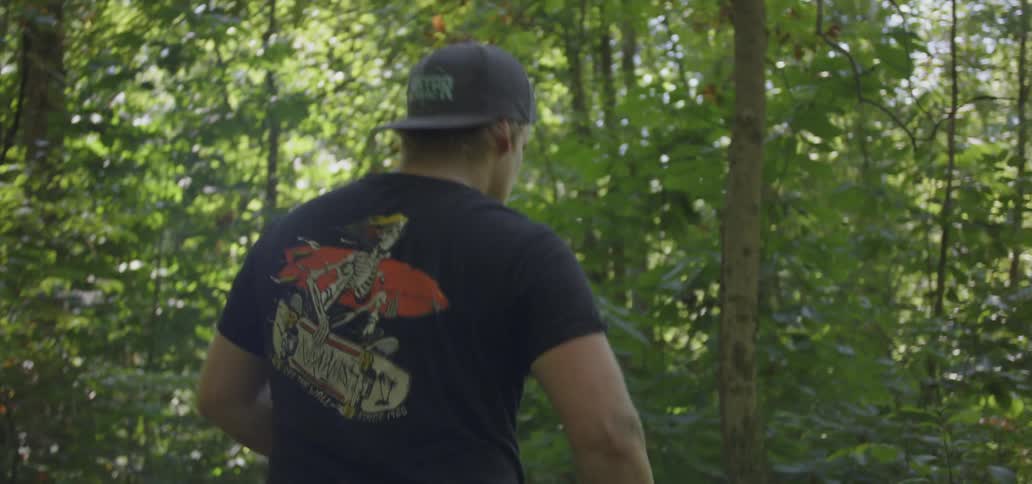 A man walks through a forest and swings a knife at plants and branches