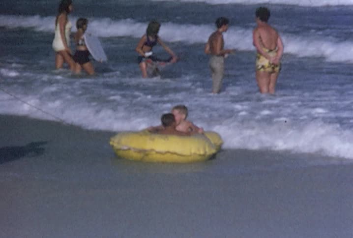 Man with children in a raft and other families at the beach