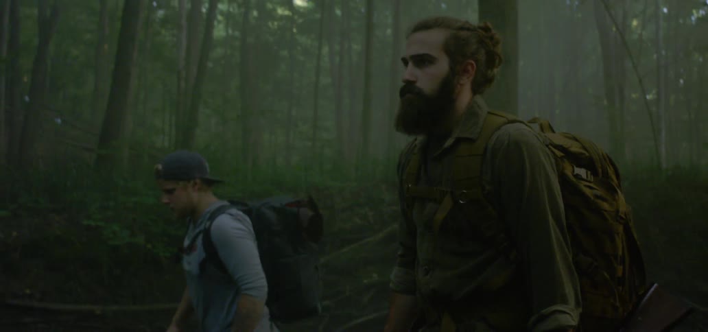 Two men walking through a river holding guns knives and backpacks