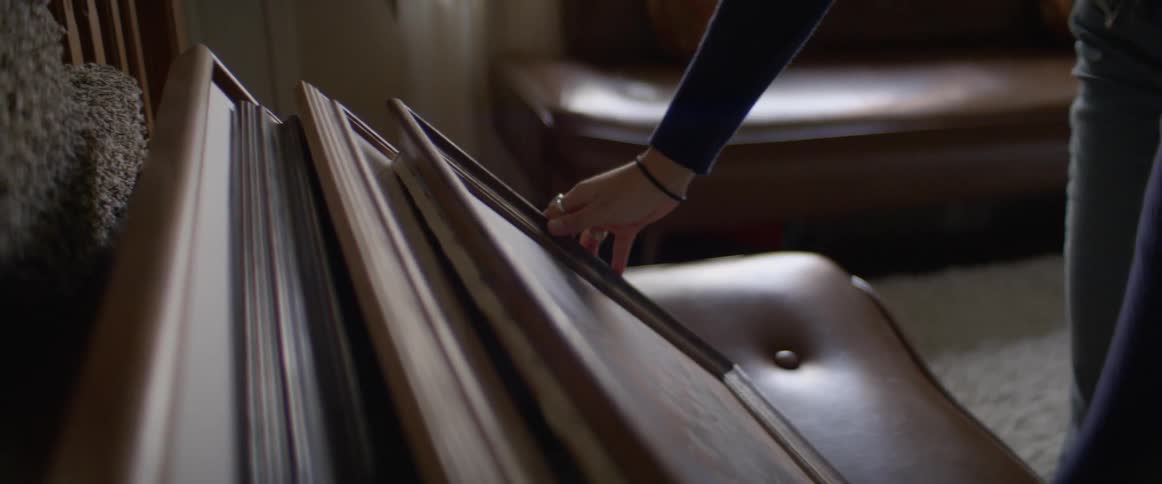 A woman places a framed painting in front of three others that are resting on a leather couch