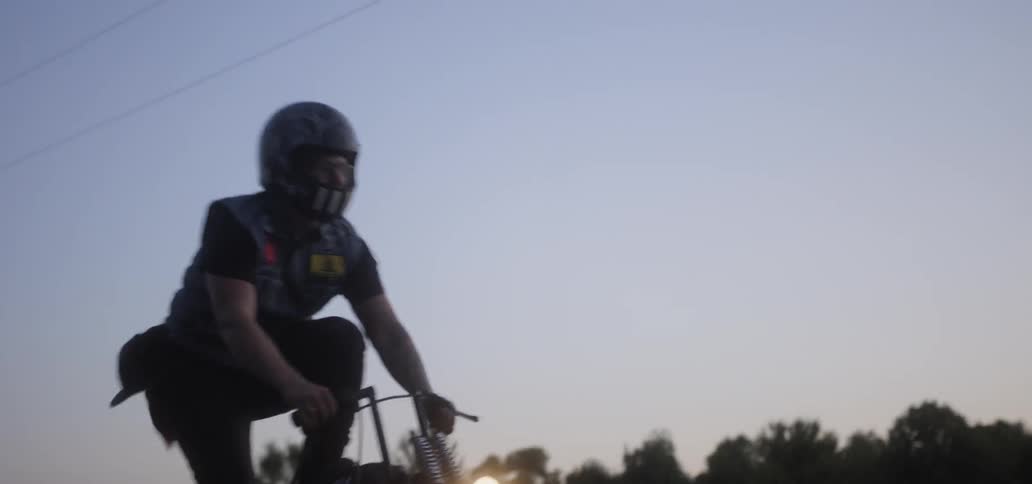 A man daringly attempts to stand up while speeding along an open road on his motorcycle