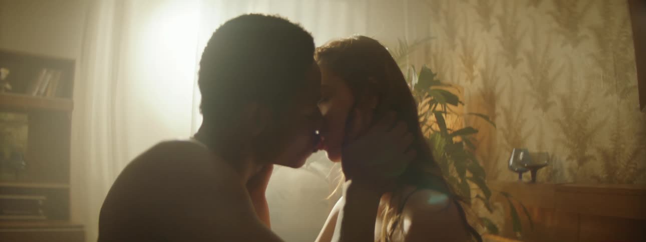 A couple frolicking on a bed as the sun streams through the window