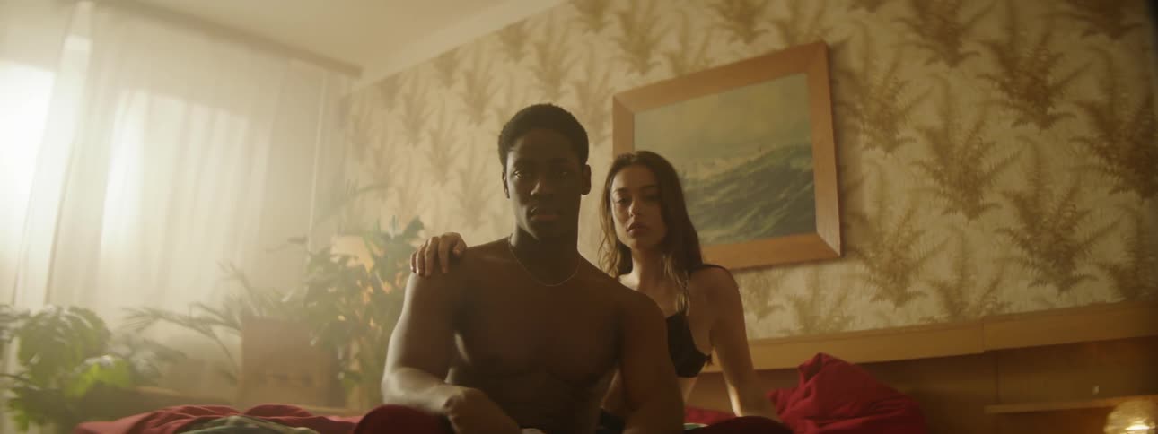 Man and woman sit on bed in wallpapered bedroom
