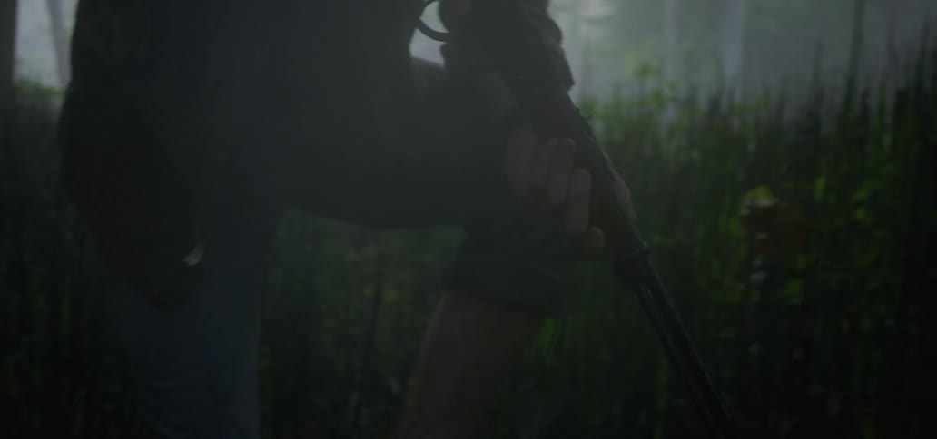 Male walks carefully through tall grass near the woods while holding a rifle