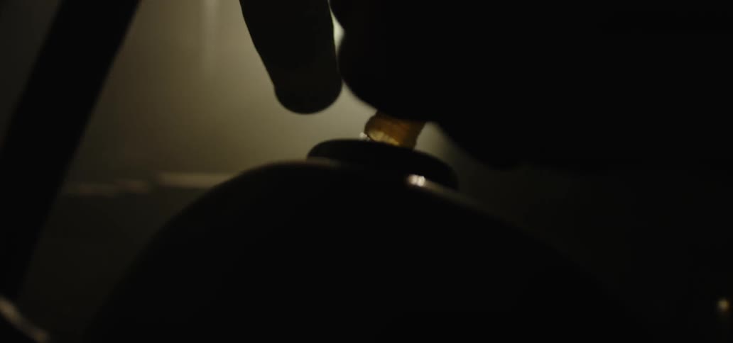 In a darked workspace a person holds a hose as liquid flows from it into a container