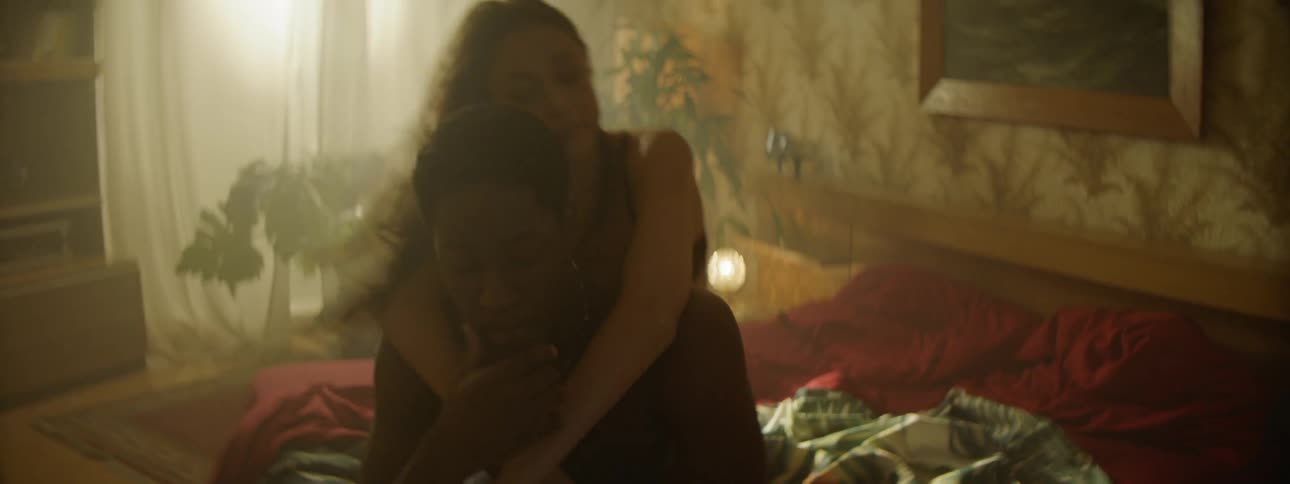 A young couple frolicking in a bedroom with floral wallpaper