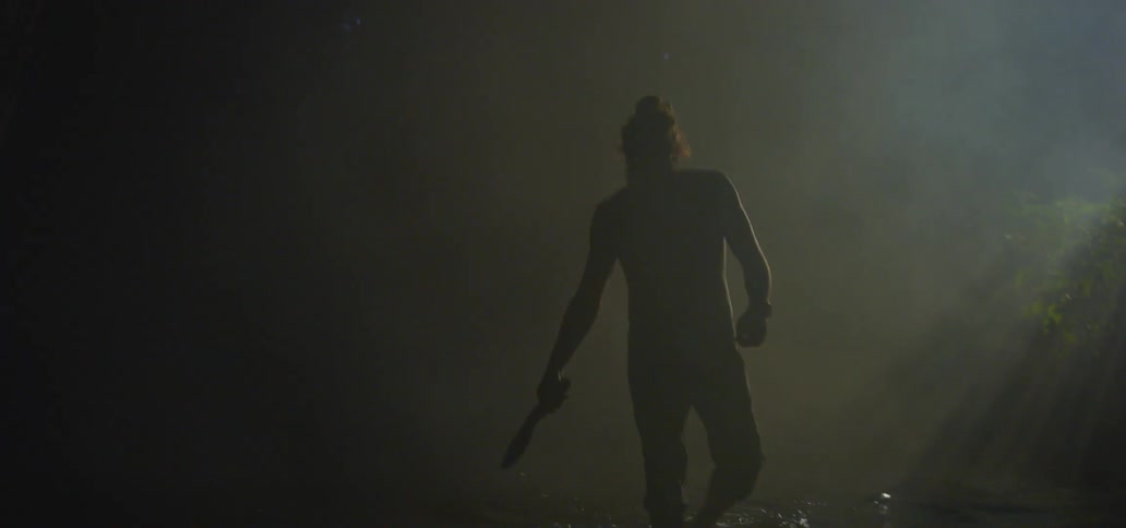 A man carrying a knife wades through a river