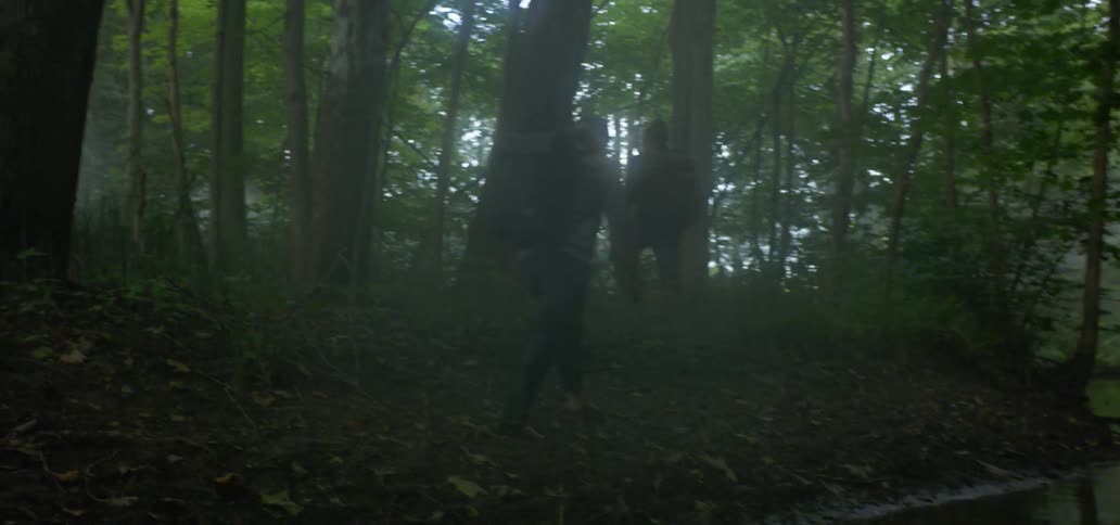 Two people hike through the woods with backpacks and bare feet
