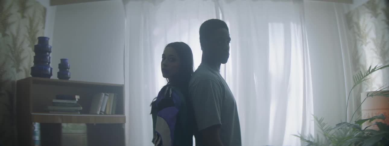A man and woman stand back to back in a room