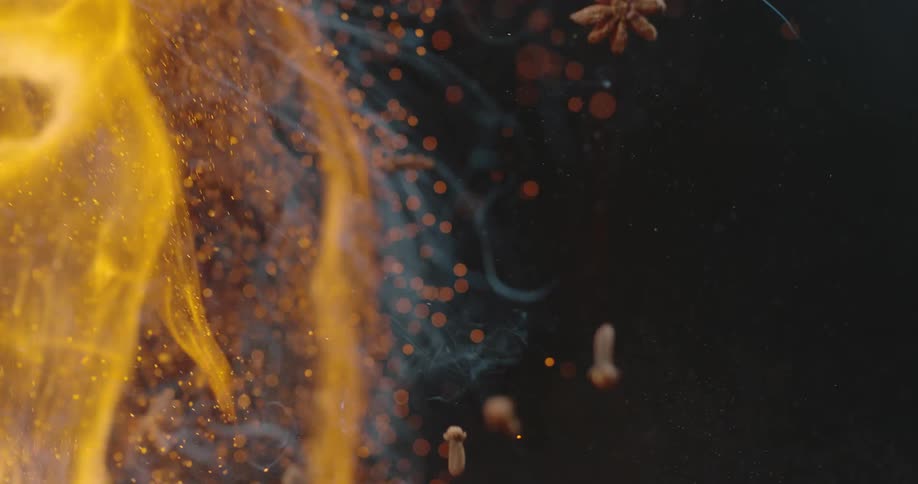 A spice and herb mixture including star anise cloves and citrus slices are tossed up and hit with flame