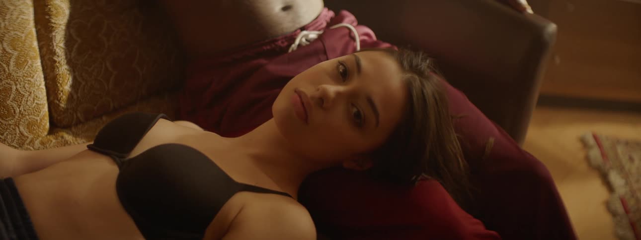 Woman wearing bra lies on couch with head in mans lap