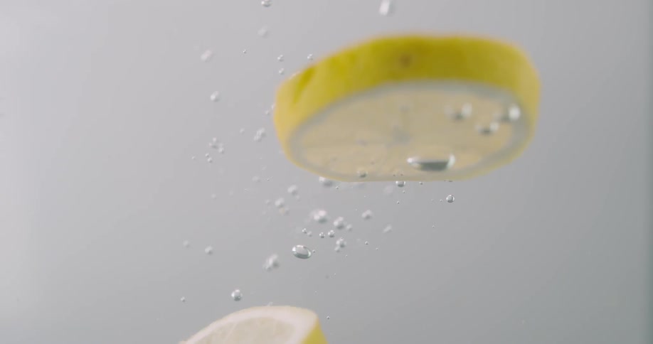 Lemon slices falling through water leaving trail of bubbles