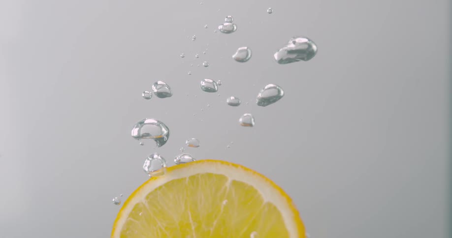 A thin slice of lemon plunges beneath the surface of crystal clear water