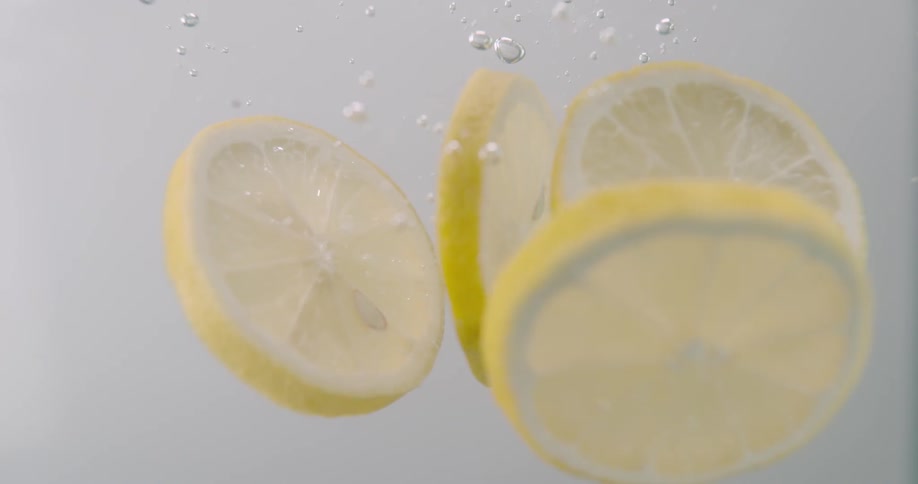 Close up of slices of lemon dropping in slow motion in water