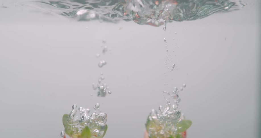 A pair of strawberries falling into a container of water