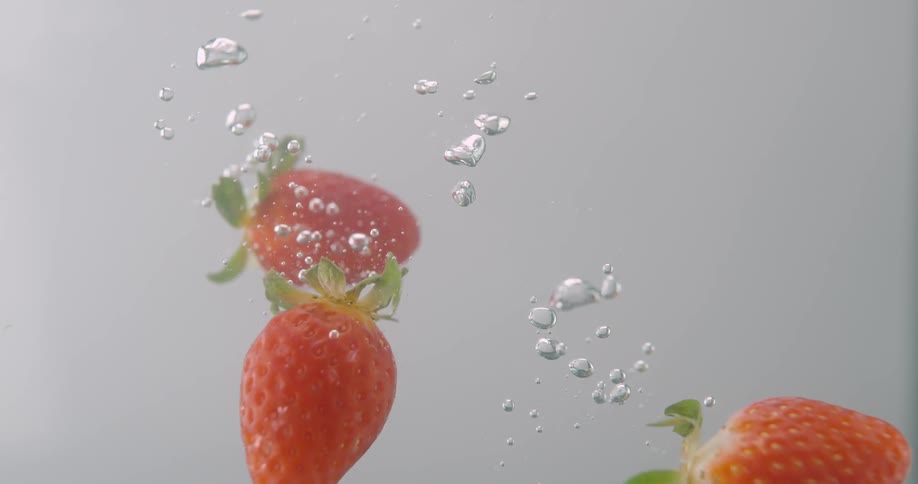 Strawberries falling in water leaving trail of air bubbles