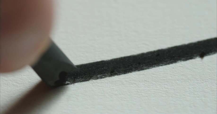 A person draws a straight black line with a piece of charcoal